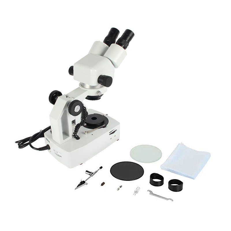 Overhead view of the JYBS gem microscope unpacked next to its technical accessories, including protective filters, replacement bulbs, and a mechanical stone holder attachment. Overhead view of the JYBS gem microscope unpacked next to its technical accessories, including protective filters, replacement bulbs, and a mechanical stone holder attachment.