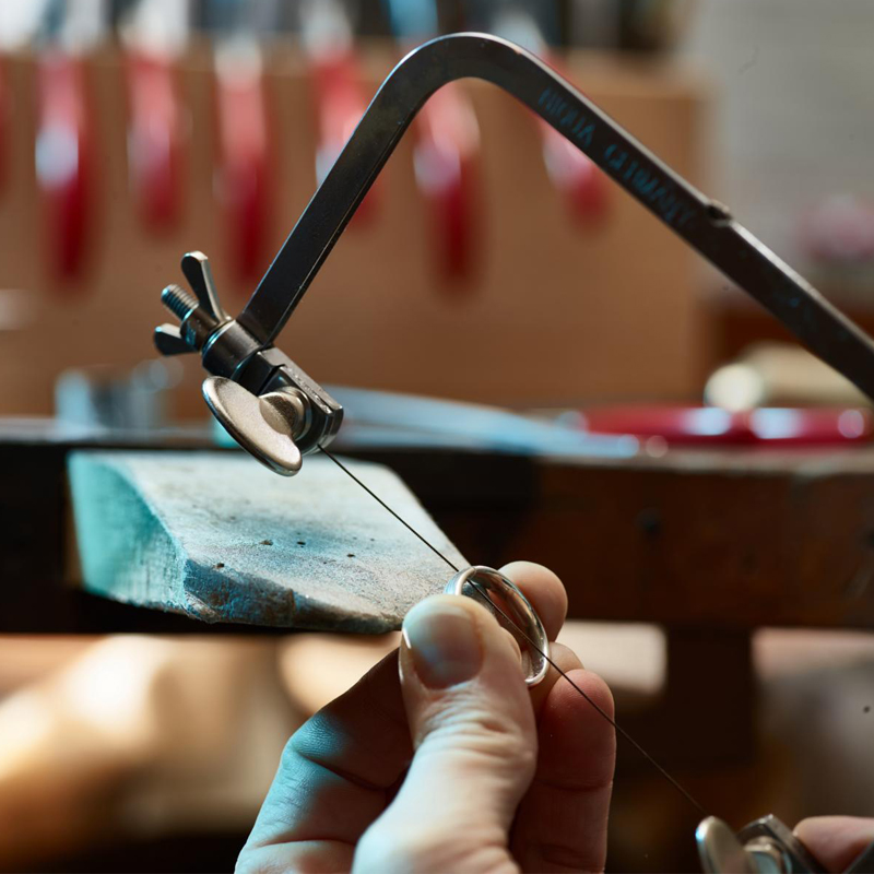 A jeweler cutting a silver ring with a jeweler's saw frame and a thin saw blade secured at both ends. A jeweler cutting a silver ring with a jeweler's saw frame and a thin saw blade secured at both ends.