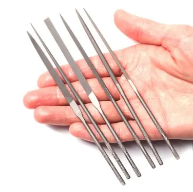 a set of six small needle files in various shapes being held in a persons palm on a white background