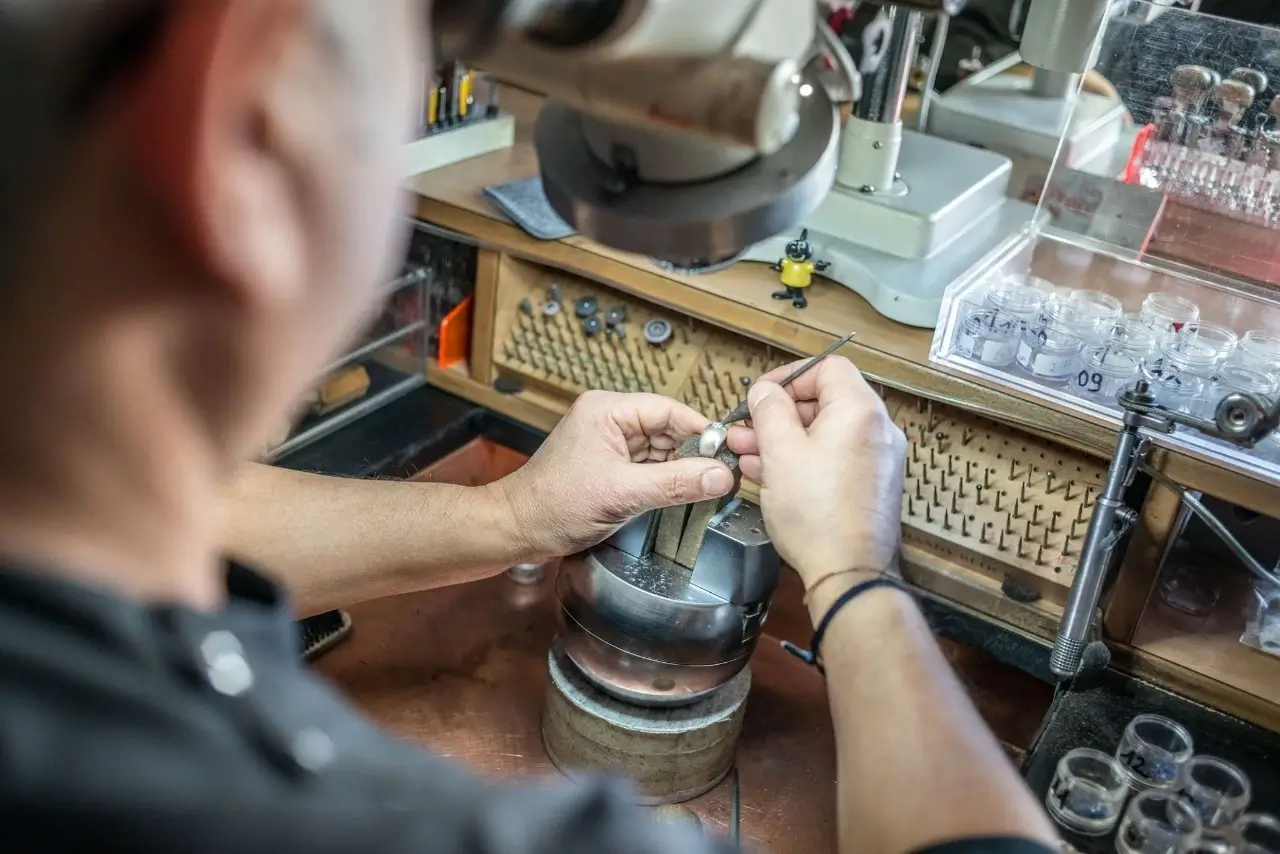 close up over the shoulder view of a jeweler setting a stone in a piece of jewelry using small tools