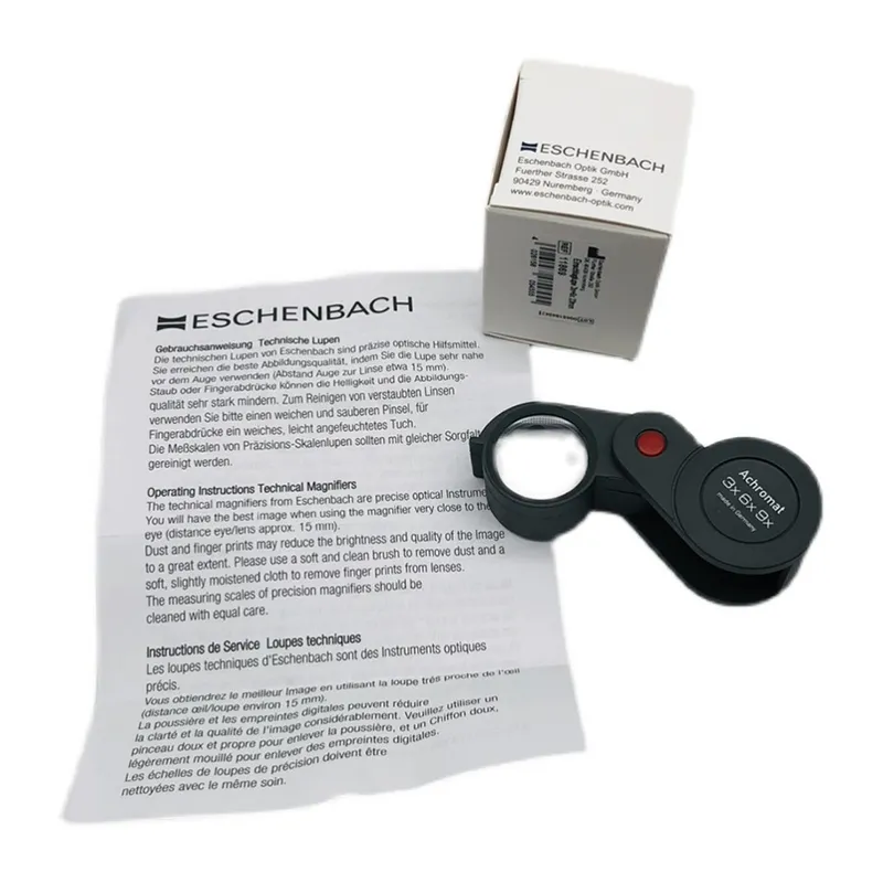 The Eschenbach folding magnifier displayed next to its original white packaging box and multilingual user manual. The Eschenbach folding magnifier displayed next to its original white packaging box and multilingual user manual.