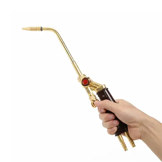 Hand holds H01-20/12/6/2 melting torch: brass/brown handle, long nozzle, red button.