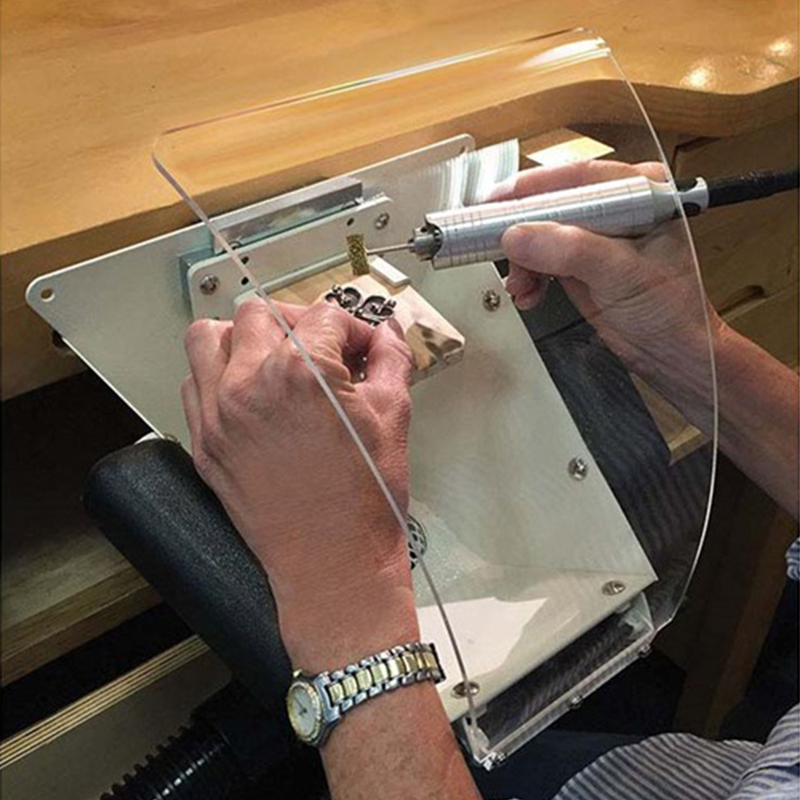 Jeweler using a rotary tool inside the Foredom Fishmouth Dust Collector with clear shield, bench pin holding jewelry. Jeweler using a rotary tool inside the Foredom Fishmouth Dust Collector with clear shield, bench pin holding jewelry.