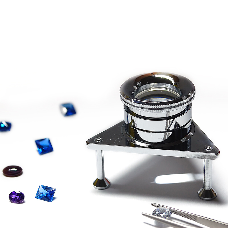 Adjustable 10x tripod loupe with a chrome finish, used for steady hands-free inspection of loose gemstones.