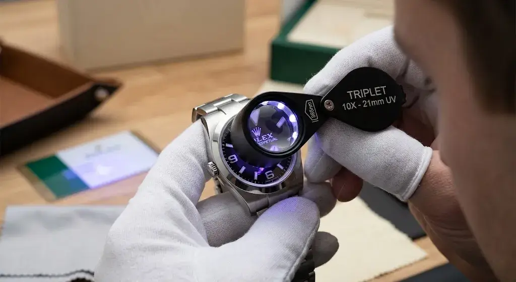Authenticator using a specialized UV 10X loupe to inspect a Rolex watch dial for security features.