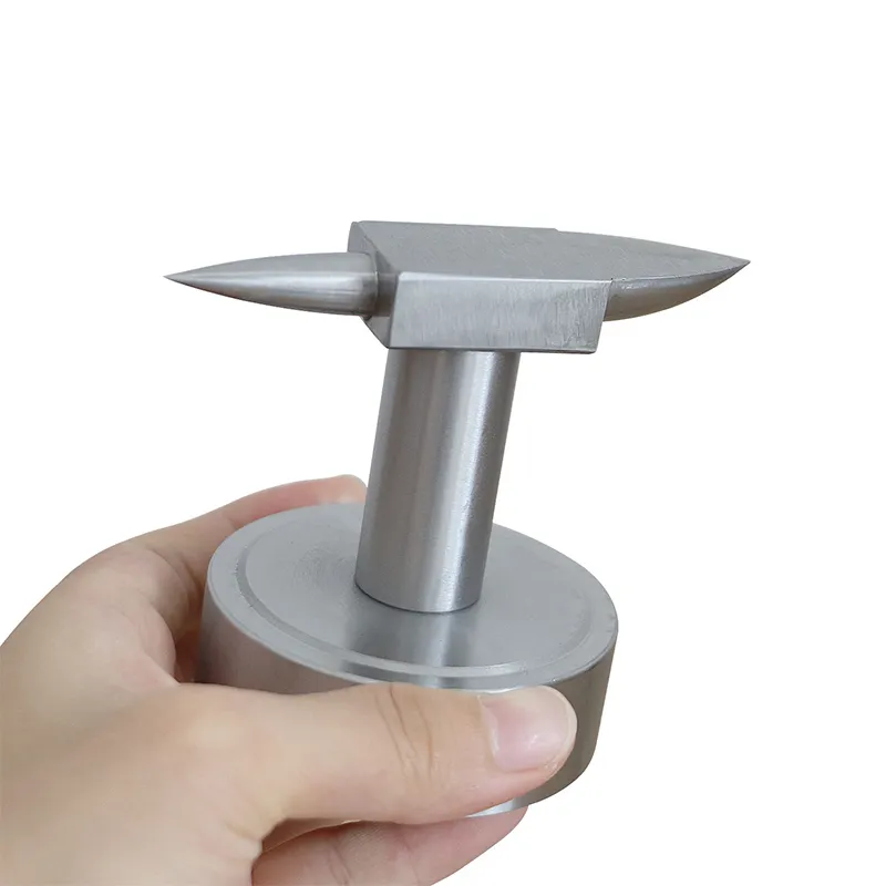 A hand holding a small steel bench horn anvil with a round base for jewelry making and metal shaping.