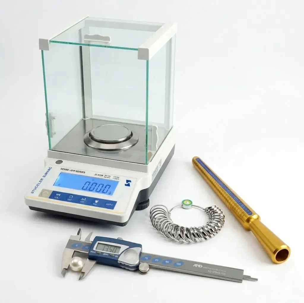 A precision digital analytical balance standing next to a brass ring mandrel, finger sizing gauges, and a caliper.