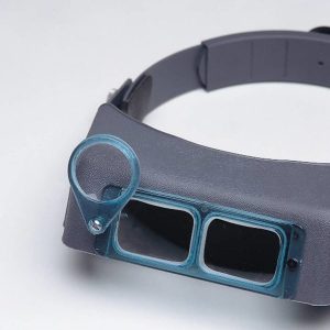 Close-up view of the blue plastic Donegan OptiLOUPE auxiliary lens mounted onto the right corner frame of a grey OptiVISOR headband magnifier.