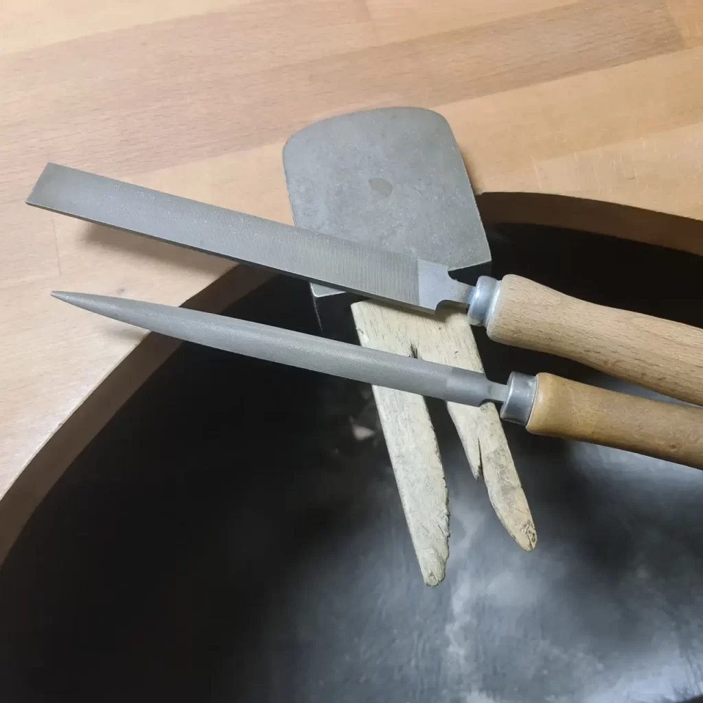 Hand precision needle files resting on a wooden jeweler's bench pin.