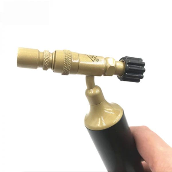 A hand grips the middle section of a gold and black butane torch, angled slightly toward the left against a white background.