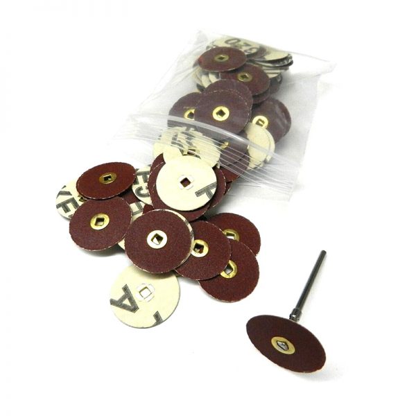A clear bag of assorted 22mm aluminum oxide sanding discs with brass centers with some scattered next to a rotary tool mandrel