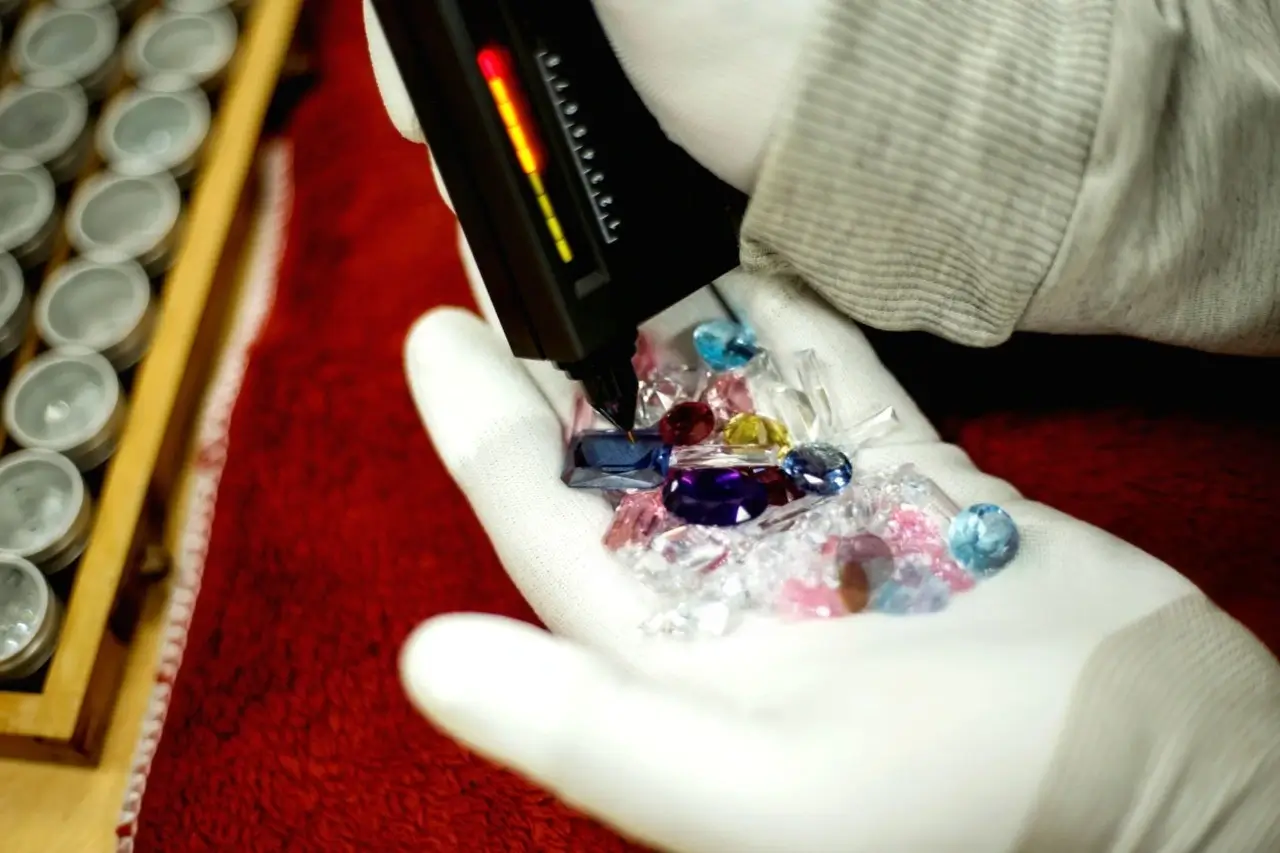 a person in white gloves tests gemstones in hand with a black diamond tester