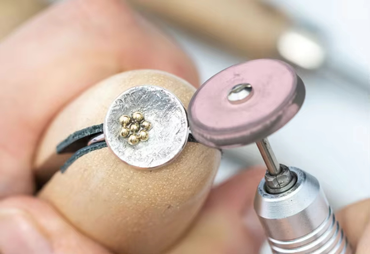 Close-up of a pink EVE UNIVERSAL polishing wheel mounted on a handpiece, polishing a silver ring