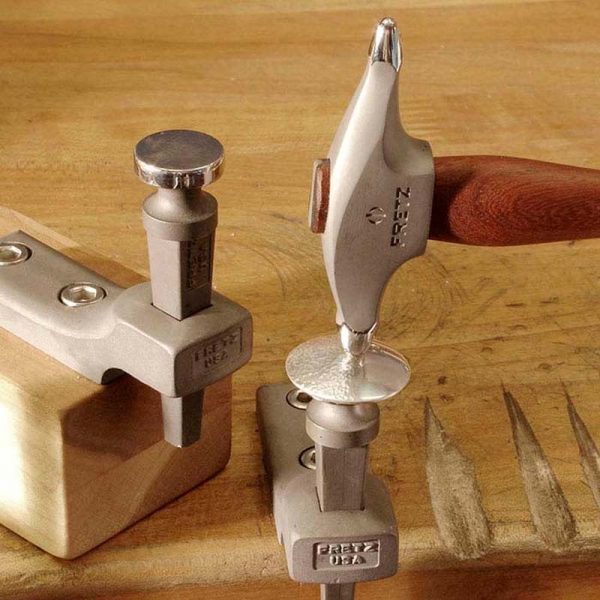 Fretz® Small Embossing Hammer in use, shaping a silver piece on a metal stake on a jeweler's bench