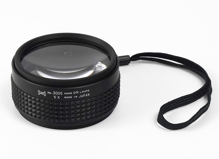 A black 5X Hand Grip Loupe with a lanyard, showing the text "No. 3005 HAND GR LOUPE 5 X MADE IN JAPAN"