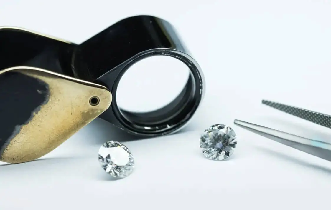 a black jeweler s loupe two sparkling gemstones and a pair of tweezers