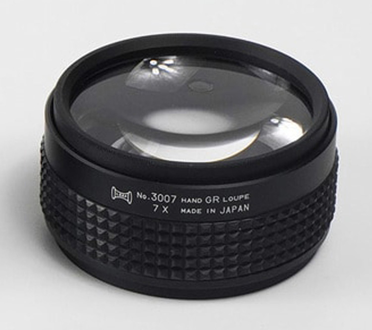 A close-up of a 7X magnification Hand Grip Loupe, showing the "7 X" and "MADE IN JAPAN" text on the side