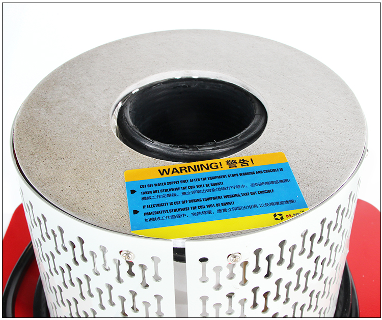 A close-up shot of the induction heating coil and crucible area with a prominent safety warning label