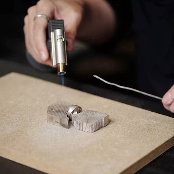 A craftsperson using a torch on a Stucler Skamolex soldering board to heat a ring for jewelry making
