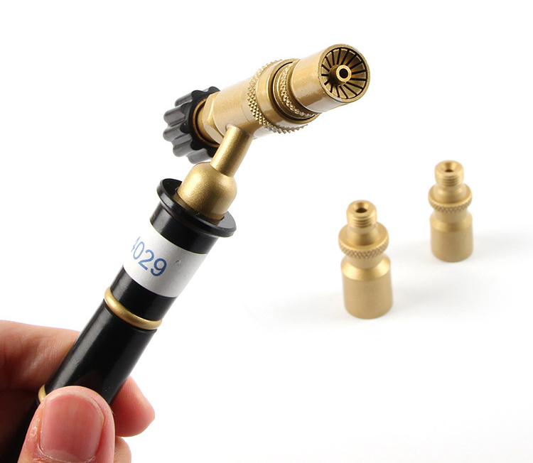A hand holding the ORCA M75 CMK torch body with two small brass nozzle tips visible nearby on a white surface