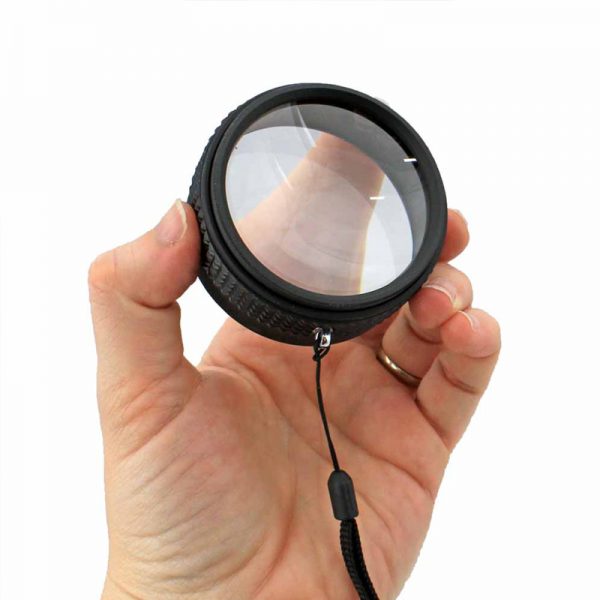 A hand holds a black magnifier loupe with a clear lens and a black lanyard attached