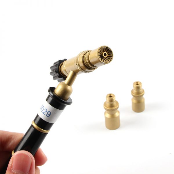 A person holding the ORCA M75 torch showing the brass tip and a black control knob with two spare tips in the background