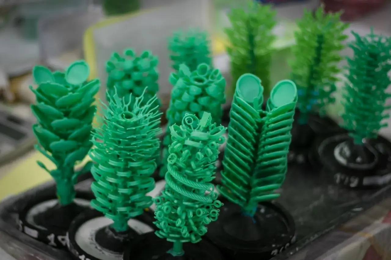 a collection of green wax models resembling trees with various jewelry pieces attached used for inve