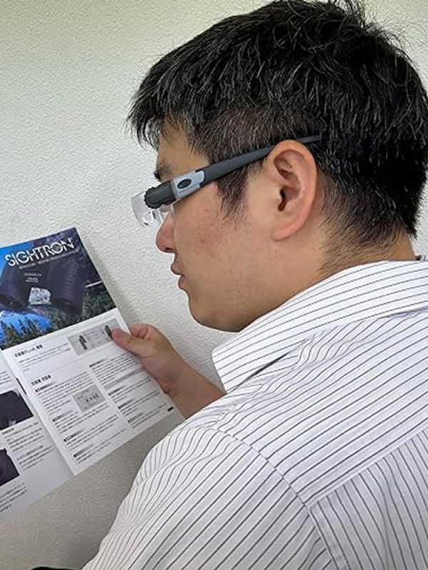 A man wearing the Eschenbach MaxDetail headset magnifier while reading, demonstrating its hands-free use.