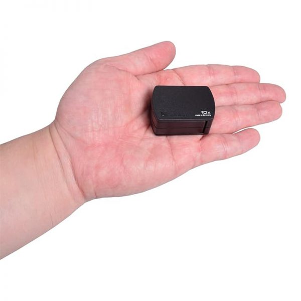 A small black Eschenbach 10x pocket magnifier sitting in the palm of a hand for scale.