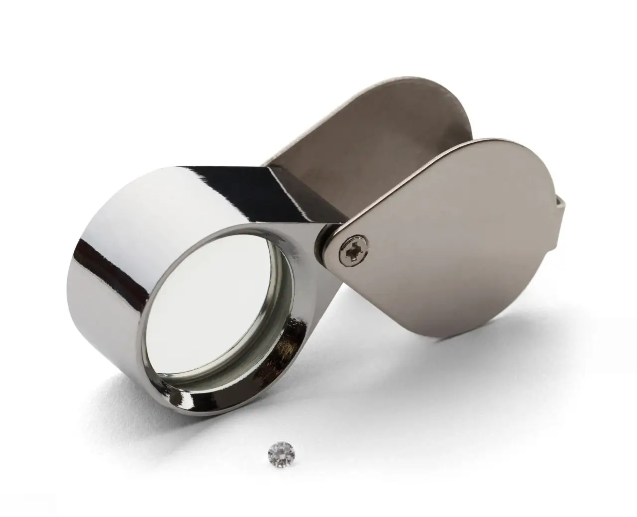 A chrome, foldable jeweler's loupe (magnifying glass) next to a small, cut diamond on a white background.
