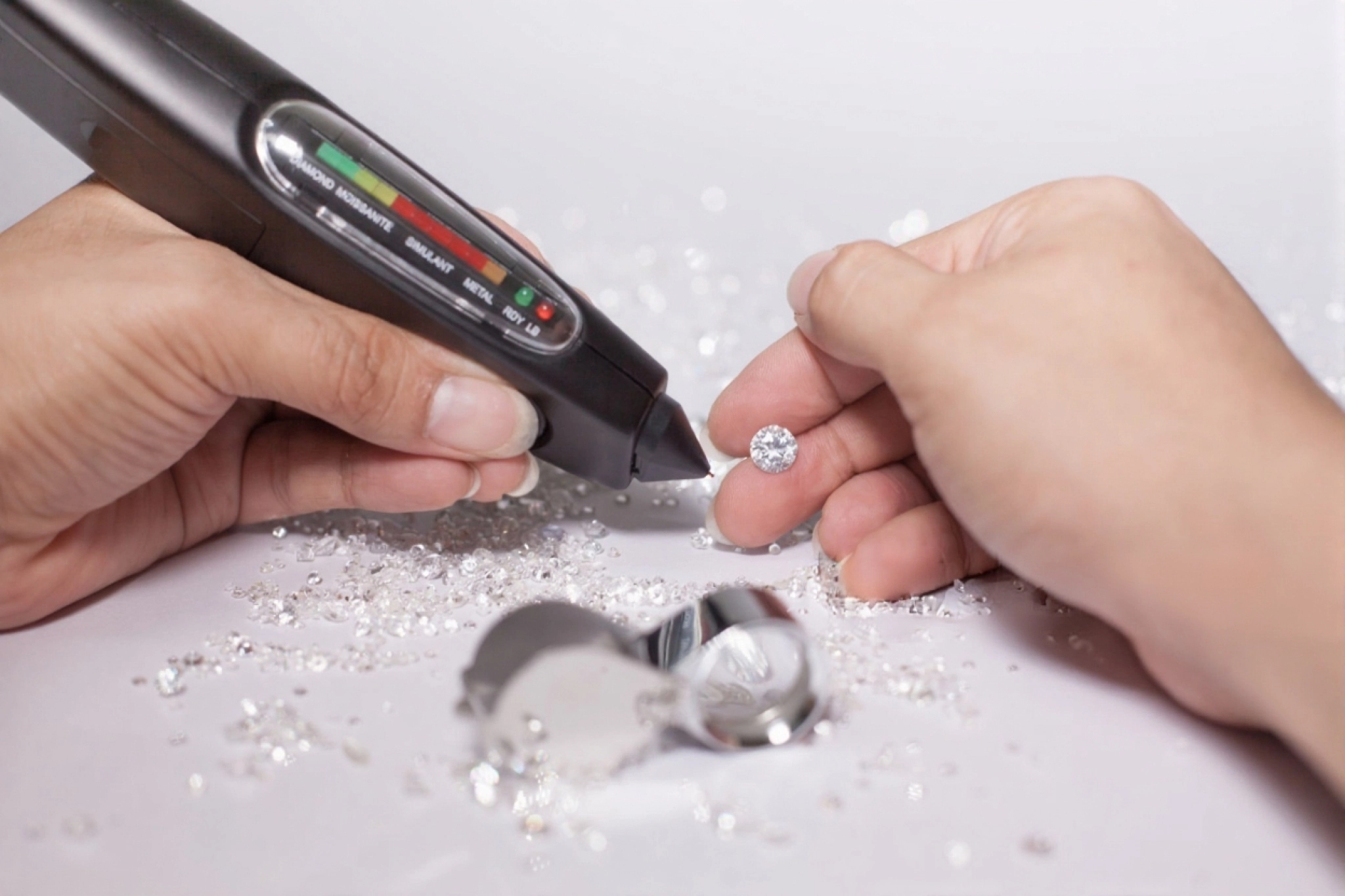 a close up of a person using a diamond and moissanite tester to check a brilliant cut gemstone surro