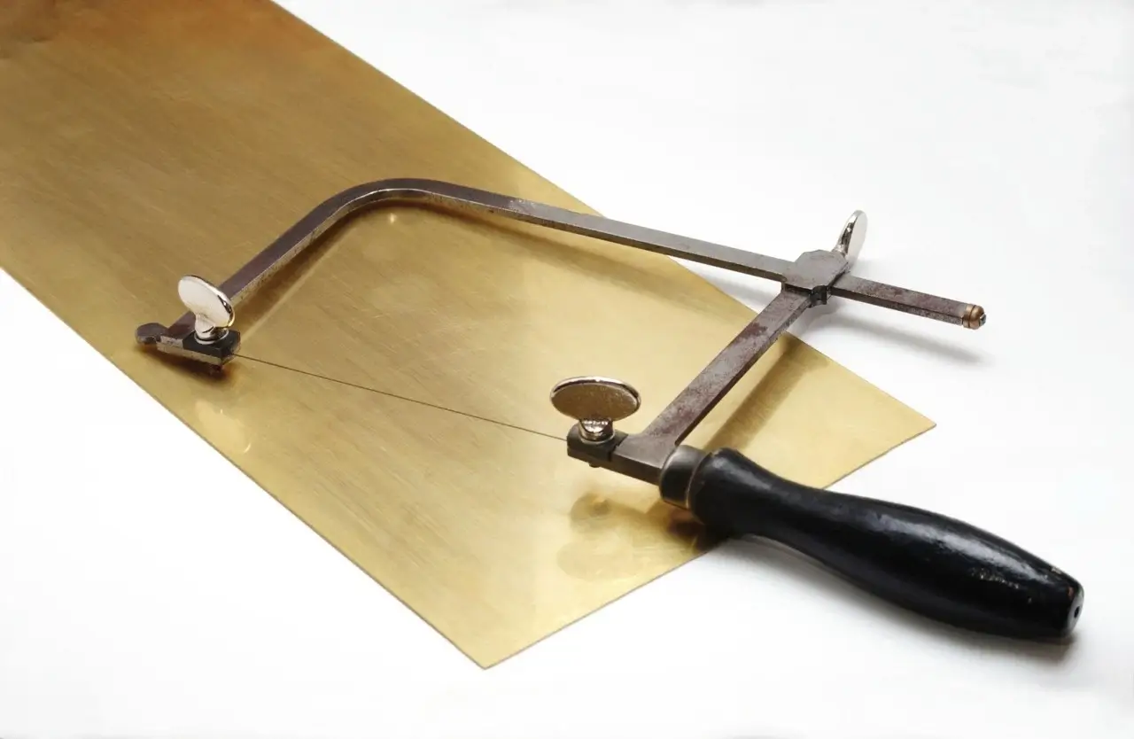 Jeweler's saw with a thin blade, housed in an adjustable metal frame, featuring a black handle, and photographed against a white background.